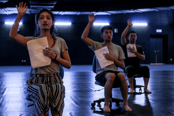 Three actors sitting seperately with their hand raised on stage. photo: Gecko