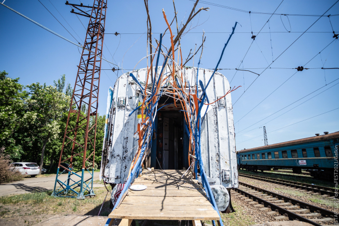 A train carriage on train tracks with a colourful structure at its entrance