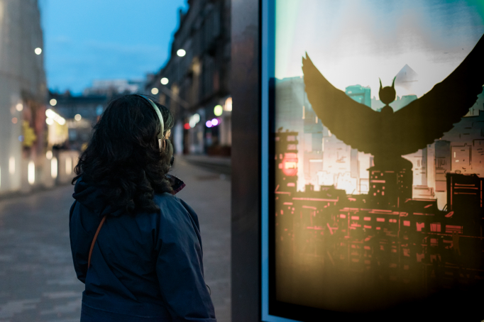 The back of a women, wearing headphones, in a city street at night with lights