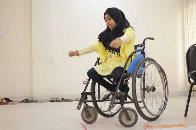 A woman in a wheelchair looks down, concentrating, and stretches out her arms