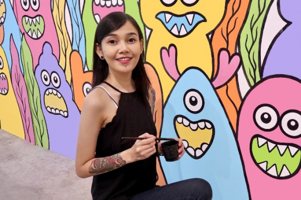 Hana Madness kneels in front of a mural, holding a paintbrush